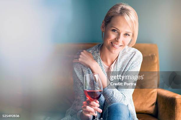 happy woman holding glass of red wine on sofa - 30 year old pretty woman stock pictures, royalty-free photos & images