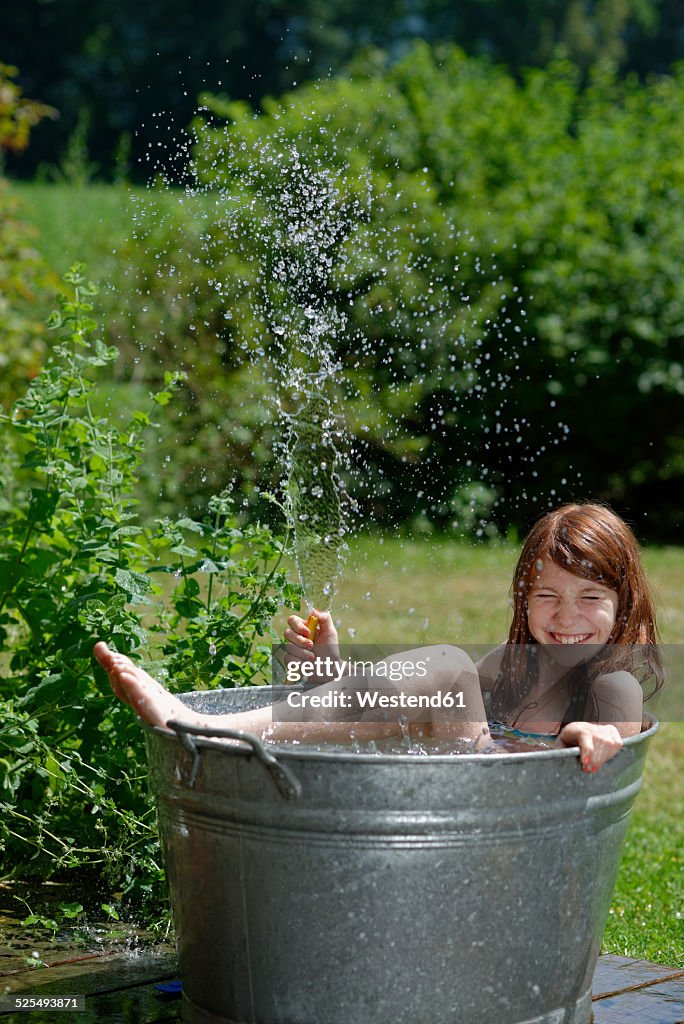 Girl holding garden hose while bathing in a zinc tub