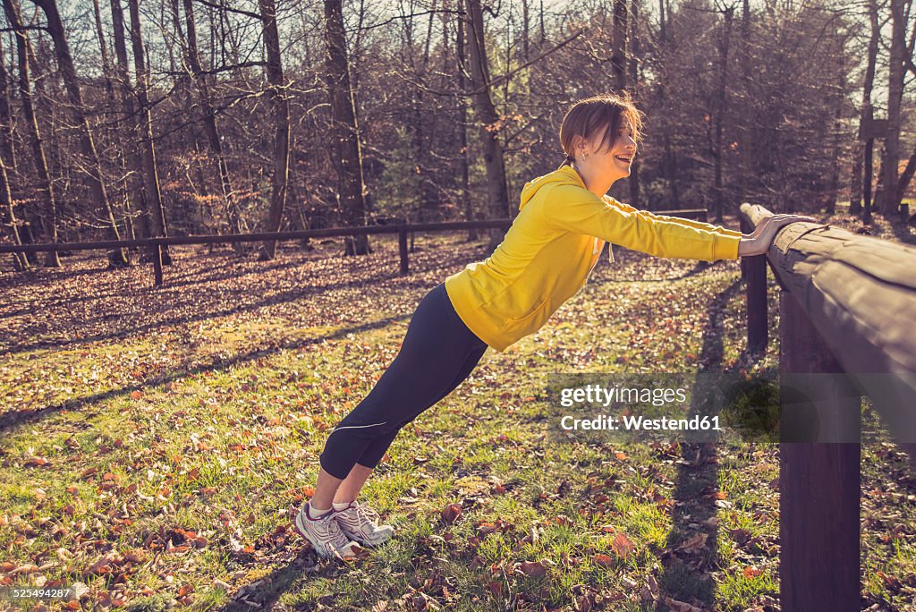 Germany, Hesse, Lampertheim, Woman doing sports in forest, Pushup on a wooden railing