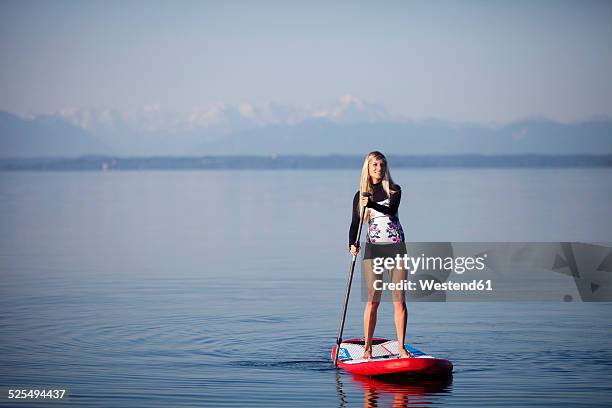 germany, bavaria, young woman standing on stand up paddle board at lake starnberg - starnberger see stock-fotos und bilder