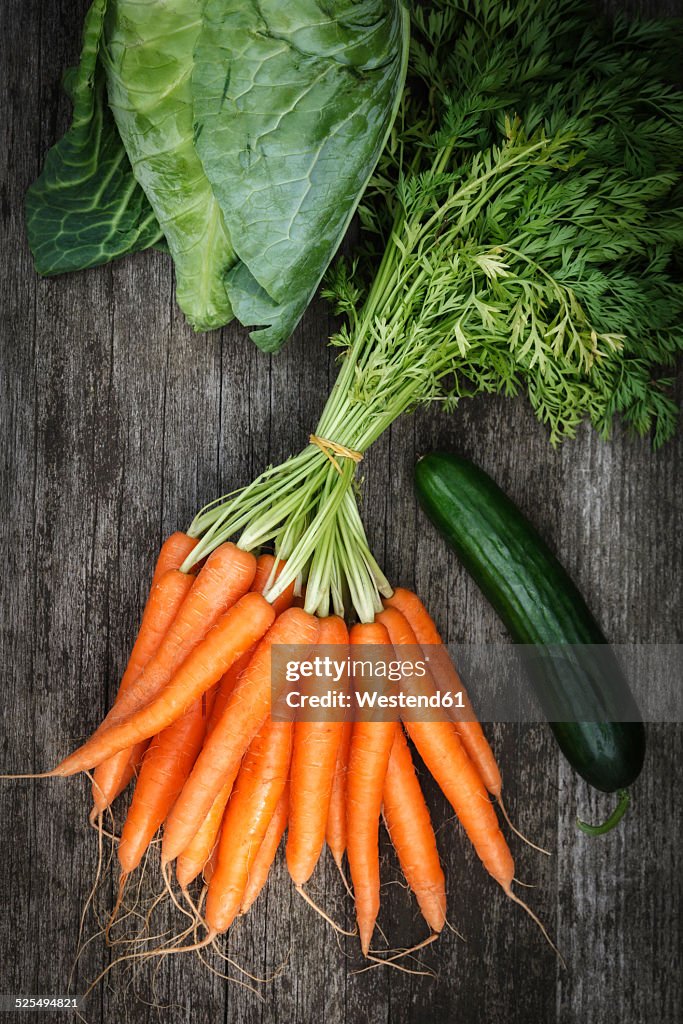 Bunch of carrots, sweetheart cabbage and cucumber on wood, elevated view