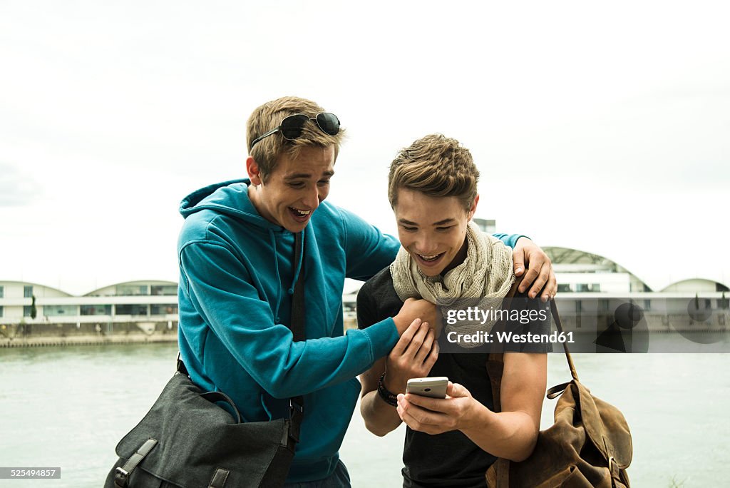 Two happy friends with cell phone by the riverside