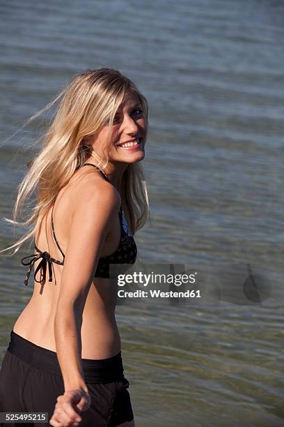 portrait of smiling young woman in front of a lake - frau haarsträhne blond beauty stock-fotos und bilder