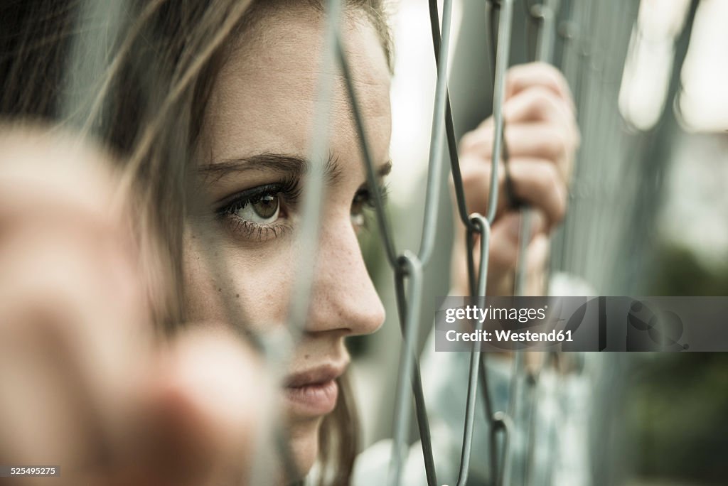 Teenage girl looking through a wire fence