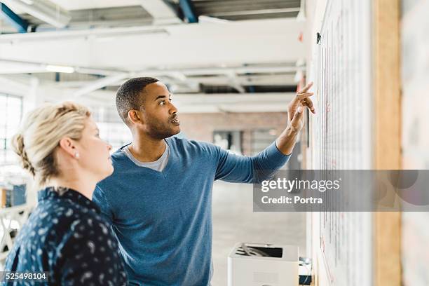 businessman discussing with colleague over whiteboard - whiteboard bildbanksfoton och bilder