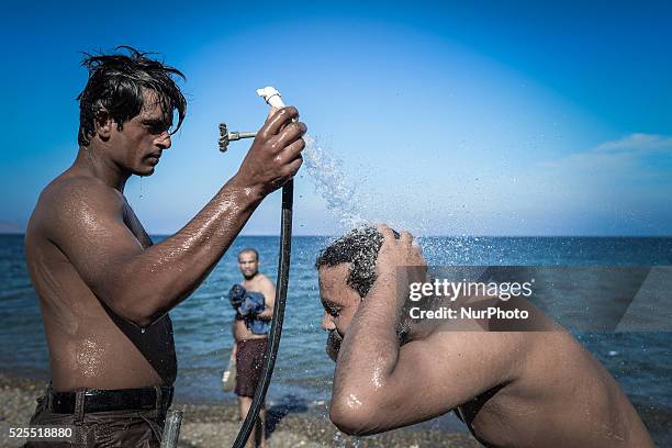 Migrants take a cold shower on the beach after a sea swimming, in Kos Town near the main Kos Police station, as they are awaiting to be processed by...