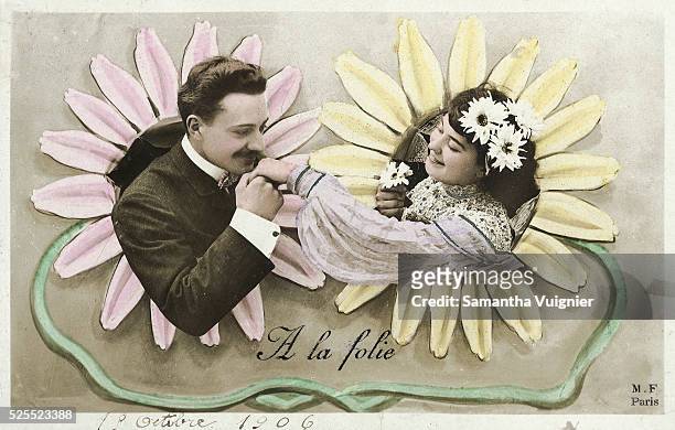 Hand-colored, real photo postcard of a romantic couple framed by painted daisies. The man is poised to kiss the woman's hand.