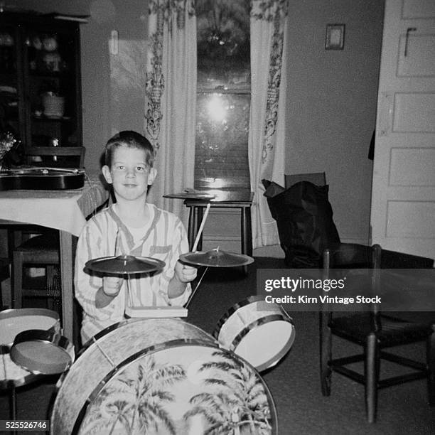 Young boy in pajamas play the drums in his living room.