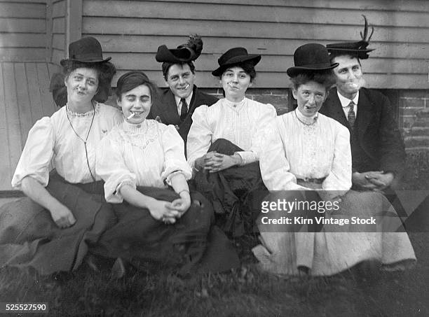 Group of young men and women wear gender reversed hats and smoke cigarettes together.