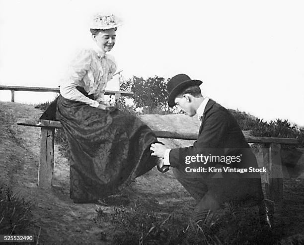 Young man on his knees adjusts a young women's shoe while she sits on a bench.