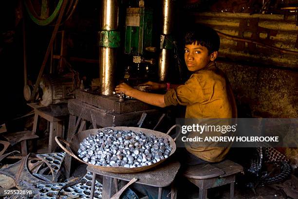 An eleven year old child laborer in a metal parts factory, where he works at a metal stamping machine with which he makes rivets. Child labor is...