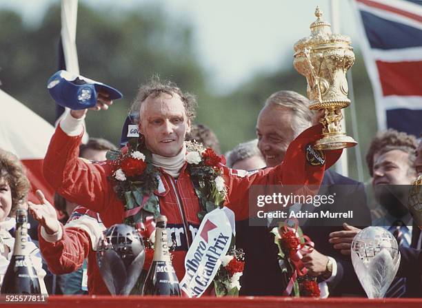 Niki Lauda of Austria and driver of the Marlboro McLaren International McLaren MP4B Ford Cosworth DFV V8 lifts the RAC Trophy and celebrates winning...