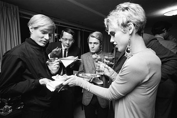 Andy Warhol and Edie Sedgwick eating hors d'oeuvres at party.