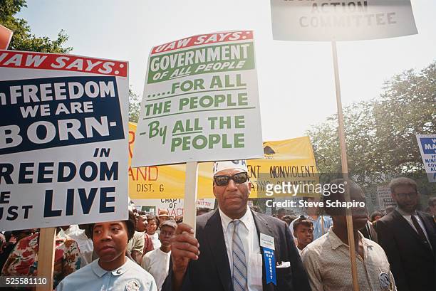 During the March on Washington, a man carries a United Auto Workers sign reading, "Government of All People, By All the People, For All the People,"...