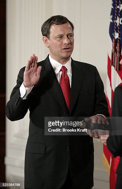 John Roberts places his hand on the Holy Bible as he is sworn in as the 17th Chief Justice of the United States during a ceremony in the East Room of...