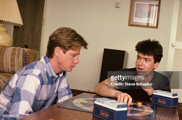 An unidentified person and Charlie Sheen at home playing the board game Trivial Pursuit.