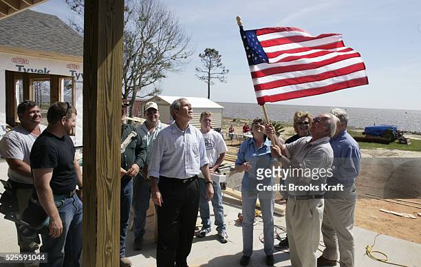 President George W Bush watches as homeowner Jerry Akins places a flag on his home as Mississippi Governor Haley Barbour and his wife Marsha look on...