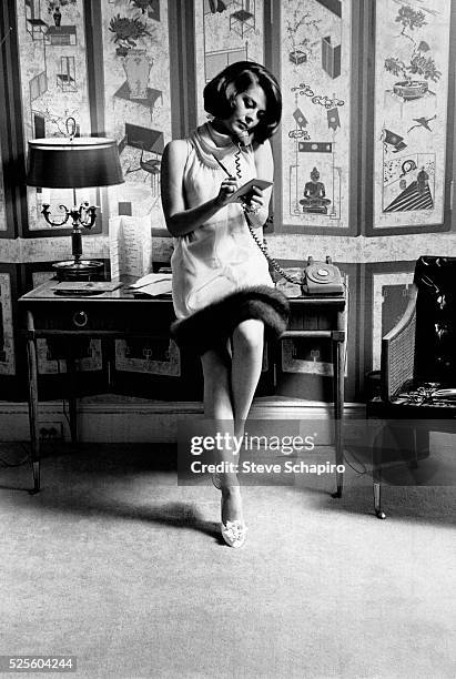 Russian-American actress Natalie Wood wearing a rollneck shift dress with a fur hem, by designer Arnold Scaasi, sitting on the edge of a desk,...