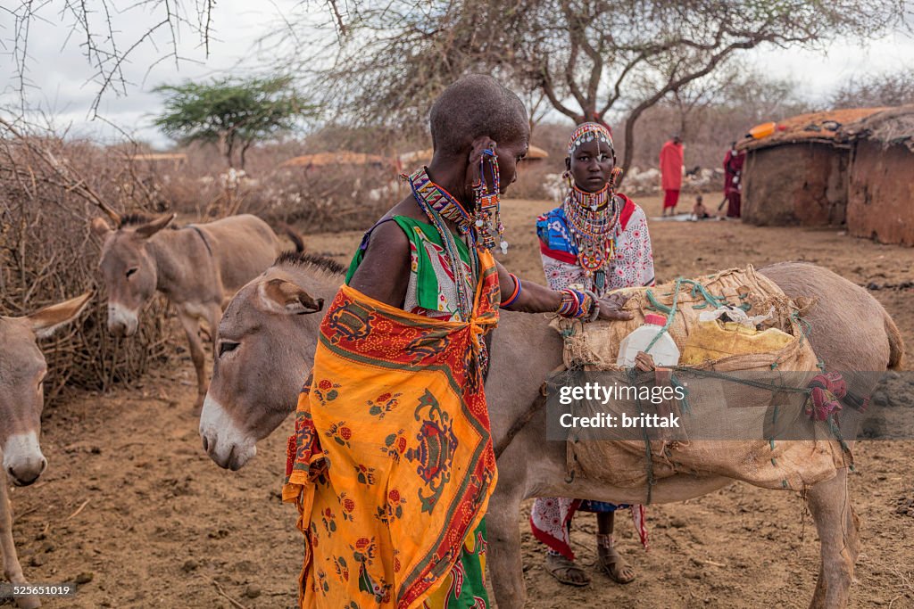 Two Maasai women loading donkey to collect water.