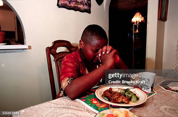 Wayne Wilson says grace before eating his dinner of chicken, broccoli, and rice alone in the dining room, after the rest of the family has already...