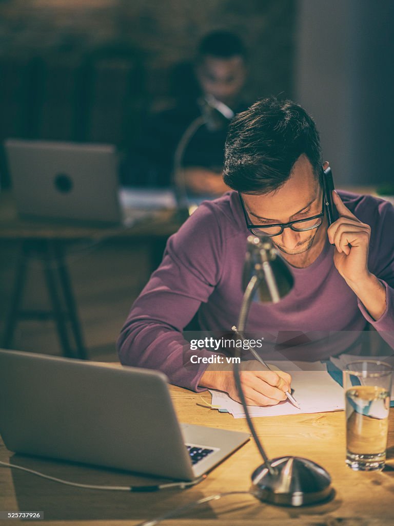 Young man using phone and writing on paper