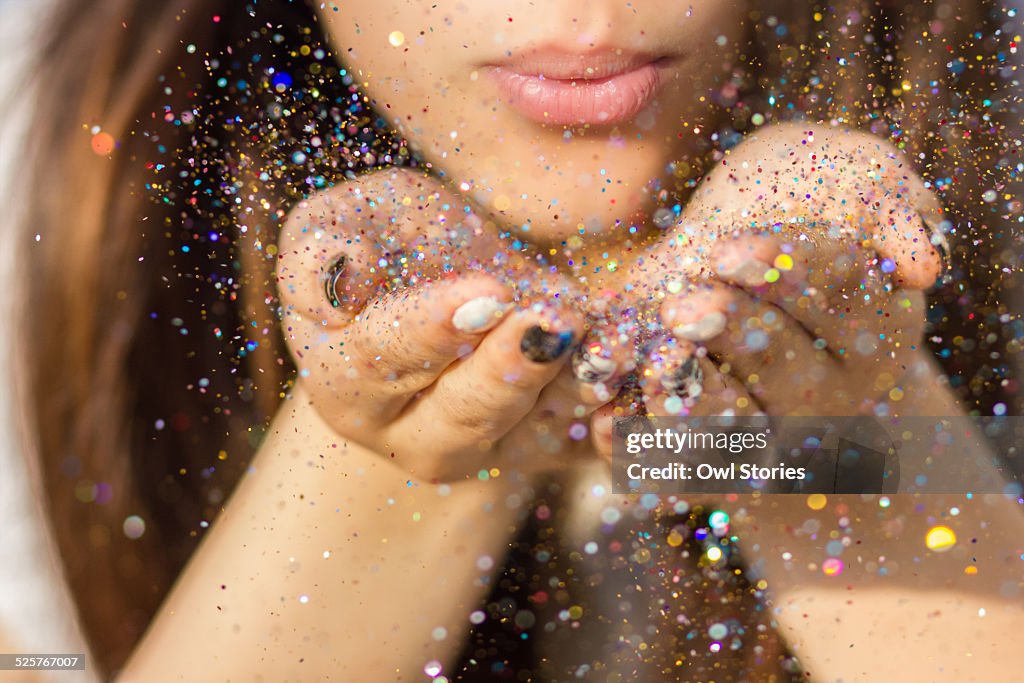 Young woman blowing colorful glitter in the air