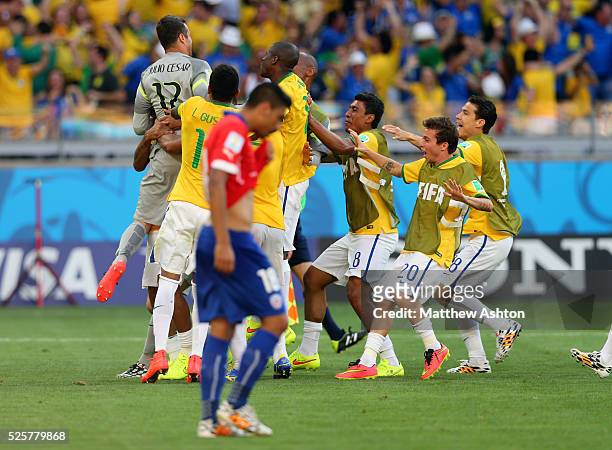 Dejected Gonzalo Jara of Chile after his penalty hits the post and Brazil celebrate earning a place in the quarter finals