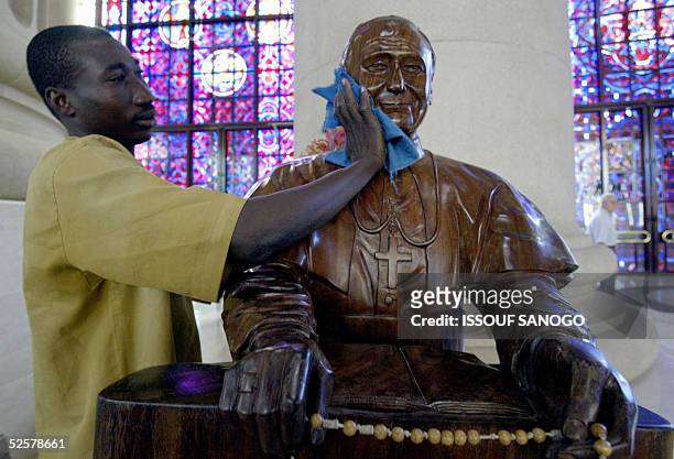 Alain Pare, an employee at Notre Dame de la Paix basilica in Yamoussoukro cleans a wooden sculpture of Pope John Paul II, prior a mass dedicated to...