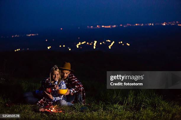 young couple having a campfire in nature at night - night picnic stock pictures, royalty-free photos & images