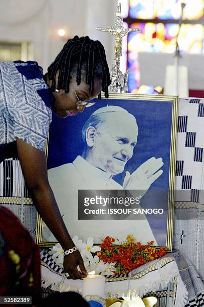 An Ivorian woman lights a candle next to a portrait of Pope John Paul II, 03 April 2005 prior a mass in Yamoussoukro's "Notre Dame de la paix"...