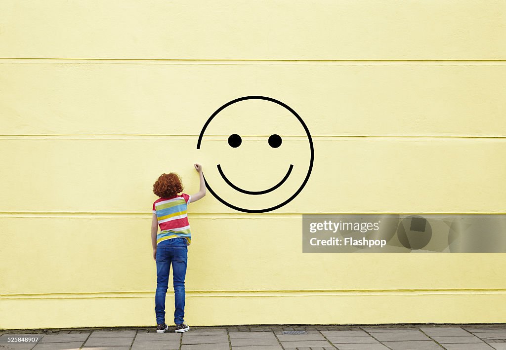 Girl drawing smiley face on to a wall