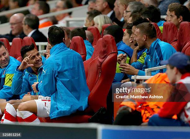 Alexis Sanchez of Arsenal pretends to take a photograph of Lukas Podolski of Arsenal as they sit on the bench