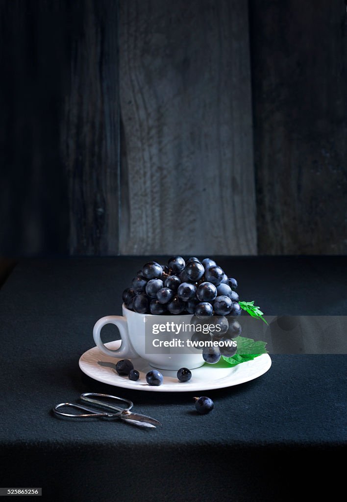 Wine grapes in white coffee cup on moody rustic wooden background. Table top view.