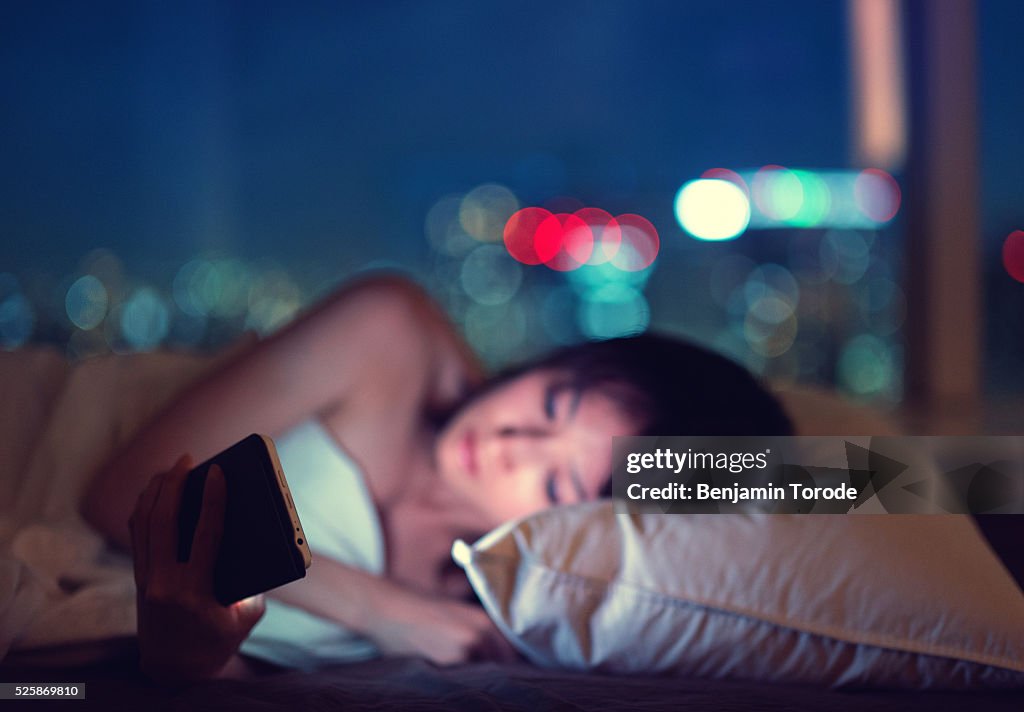 Women reading smartphone in bed at night