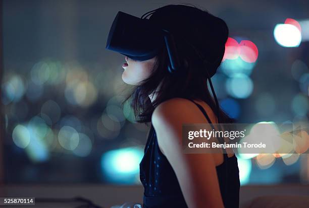 woman using virtual reality headset at night with city lights in background - virtualitytrend stock pictures, royalty-free photos & images