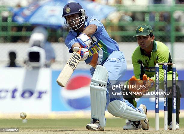 Indian cricketer Mahender Dhoni is watched by Pakistani wicketkeeper Kamran Akmal as he plays a shot during the second one day international match...