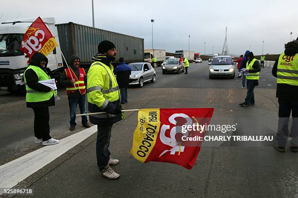 People wearing waistcoats and holding flags of the French CGT Trade Union distribute flyers as they block the road at a toll booth on the Normandy...