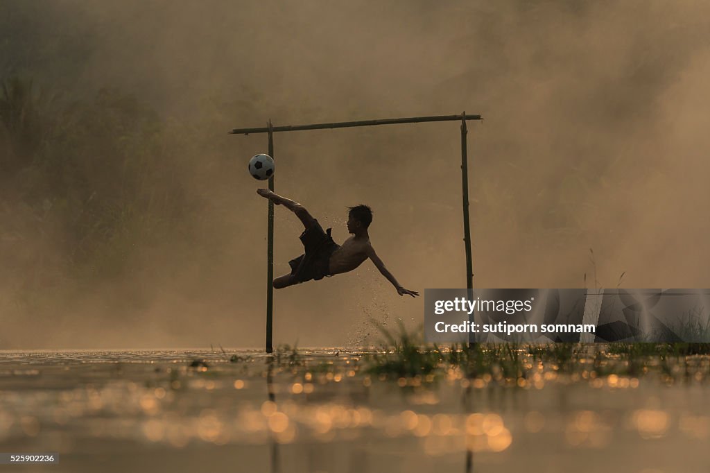 Boy playing football shooting at goal in river.