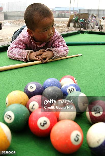 Four-year old child plays with balls on an outdoor pool table on April 5, 2005 in Beijing, China. Outdoor pool, one of the cheepest participation...