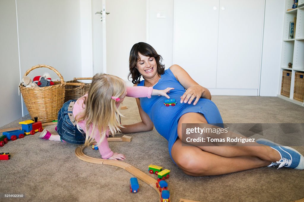 Pregnant woman and girl (2-3) playing with toy train