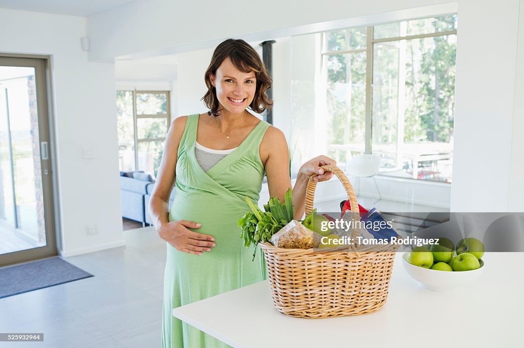 Pregnant woman holding basket with vegetables in kitchen