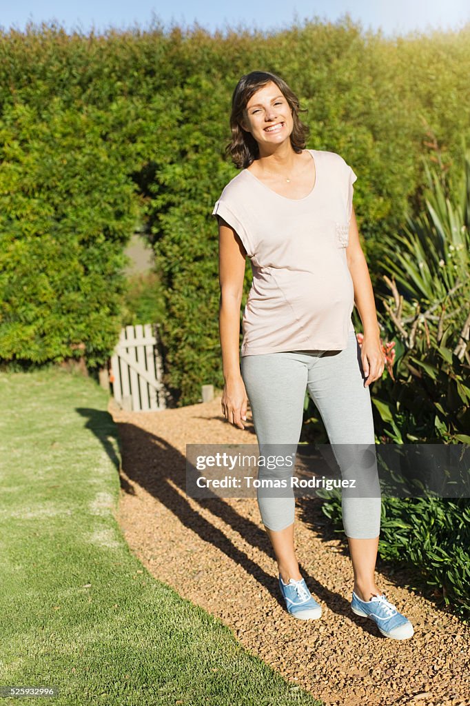 Smiling pregnant woman standing on path in garden