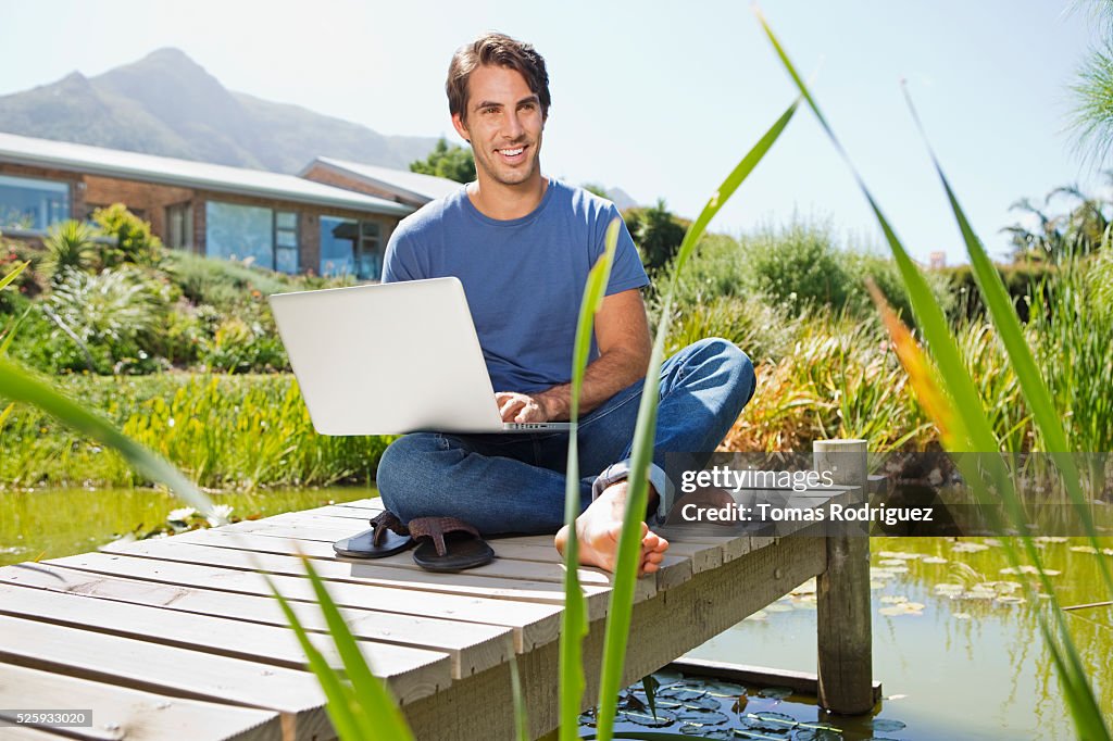 Man sitting on jetty and using laptop