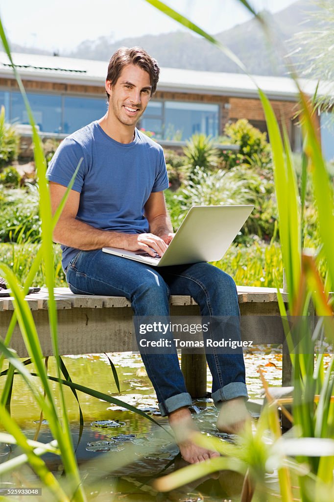 Man sitting on jetty and using laptop