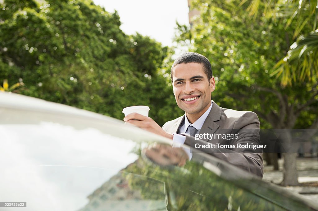 Portrait of mid adult man with coffee cup leaning on car