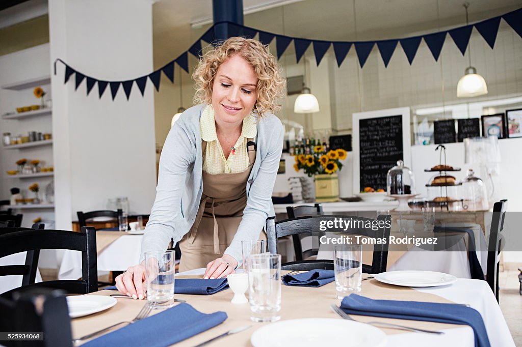 Portrait of young waitress setting table at restaurant