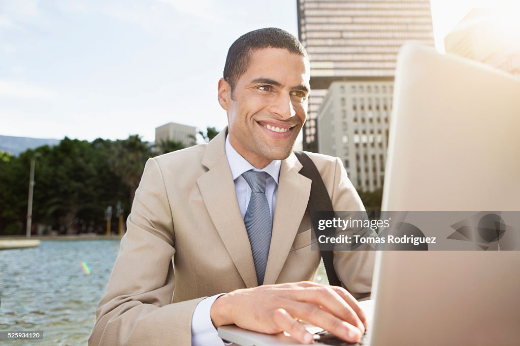 Portrait of mid adult man sitting by fountain and using laptop