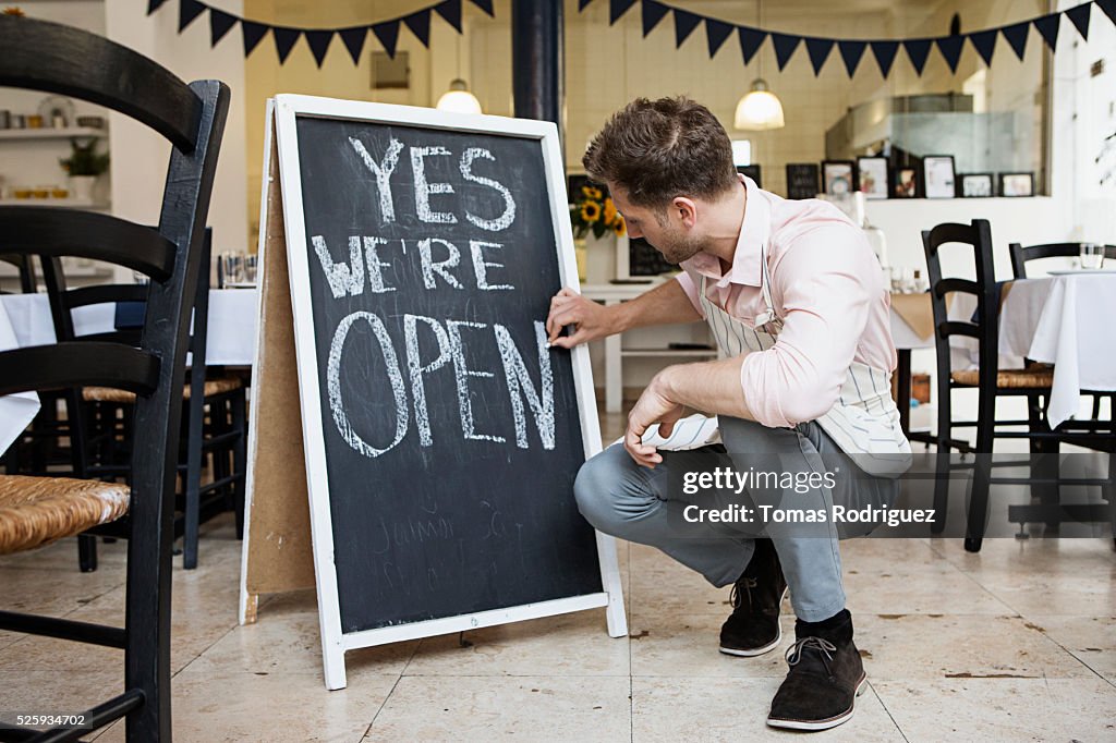 Portrait of mid adult waiter crouching by blackboard and writing