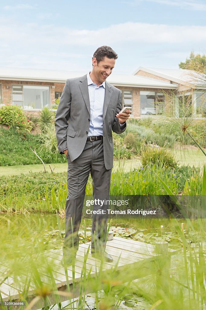 Man standing on jetty by pond in back yard and text messaging