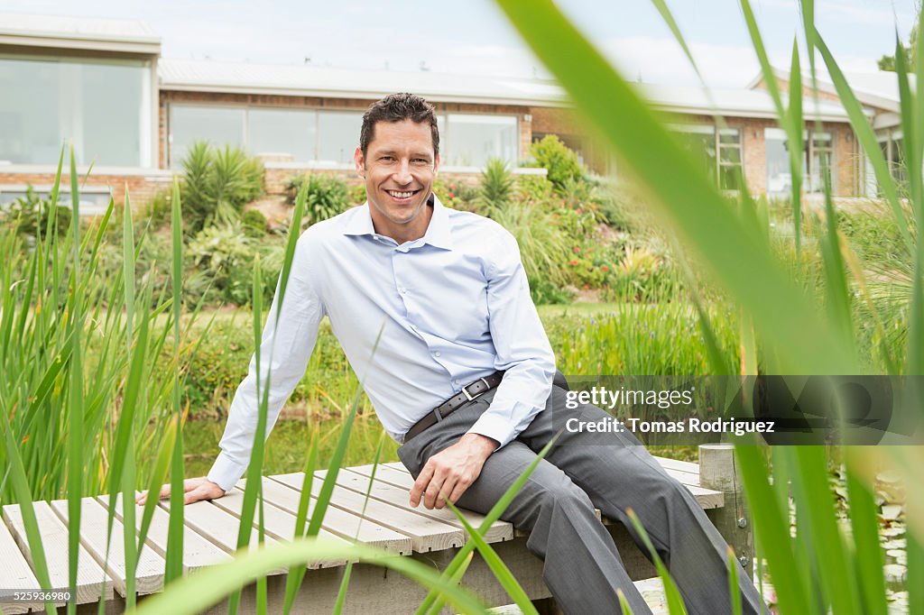 Man sitting on jetty by pond in back yard